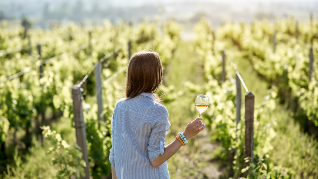 a woman standing in a vineyard in France with a glass of Rosé during a wine tourism trip